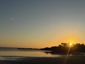 Ein Strand bei Sonnenuntergang mit einer Stadtansicht im Hintergrund.