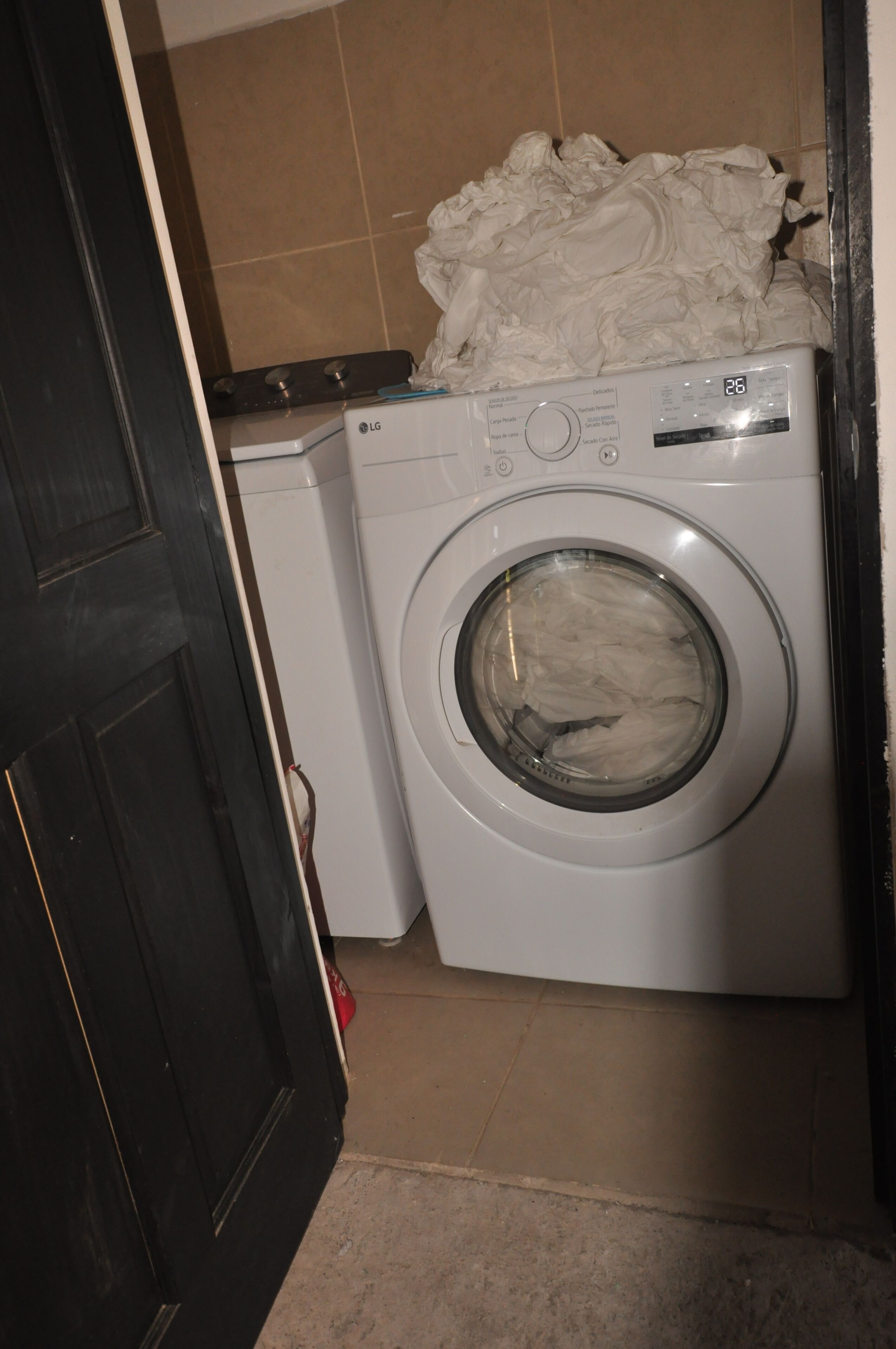 A compact, white washing machine in a small laundry room with a tiled floor and a dark door.