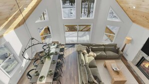 Ein modernes Interieur mit Essbereich, Sofa, Kamin und großen Fenstern.