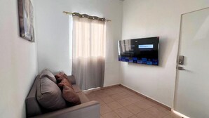 A small living room with a sofa, a television mounted on the wall, and a door.