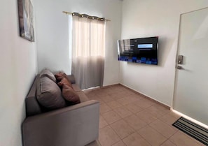 A small living room with a sofa, a television mounted on the wall, and a door.