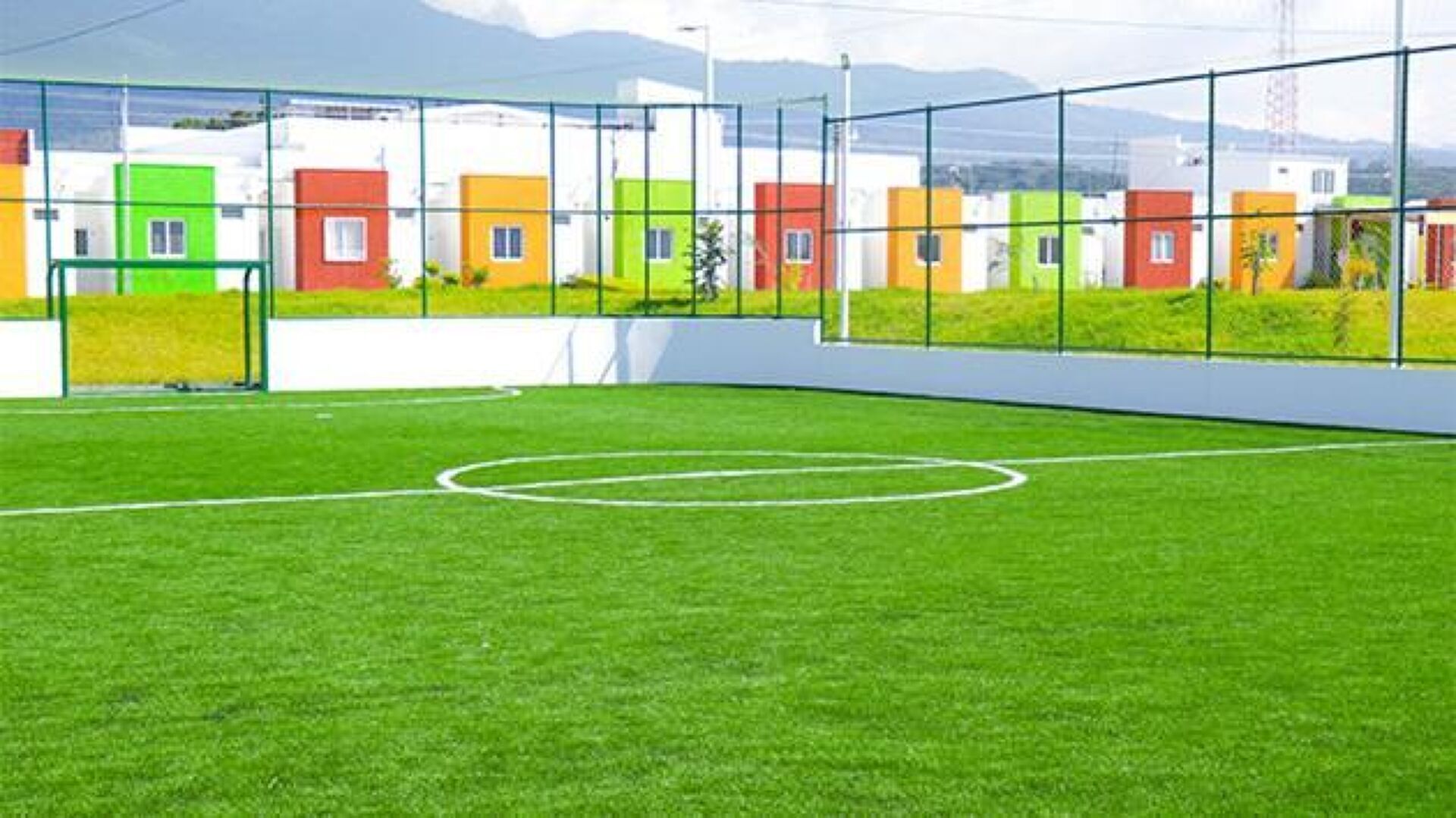 A soccer field with a goalpost and a row of colorful houses in the background.