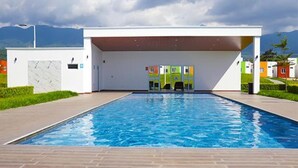 A modern swimming pool with a clear blue water surface, surrounded by a paved walkway and a building with a flat roof.