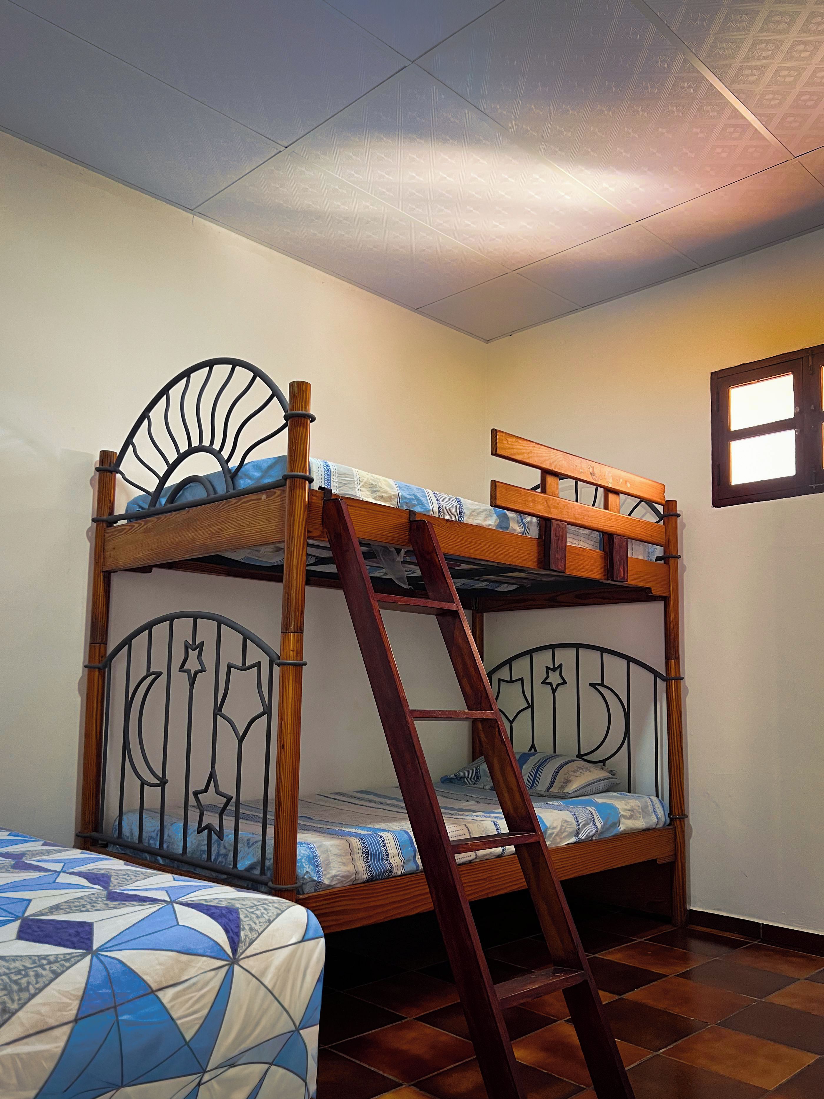 Una cama individual superpuesta con escalera, ventana y colcha estampada.