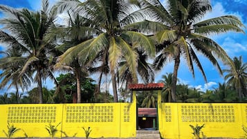 Um portão amarelo com uma pequena construção em frente, cercado por palmeiras e um céu claro.