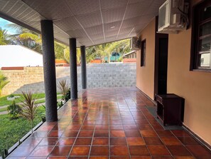 Ein überdachter Außenbereich mit gefliestem Boden, Klimaanlagen und Blick auf eine Wohngegend mit Palmen.