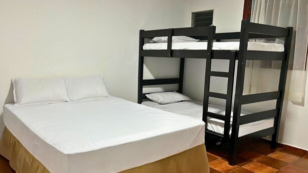 A single bed with a white mattress and a beige skirt, a bunk bed with white bedding, and a tiled floor. - Quinta Hojas de Mar - Las Hojas Beach (La paz)