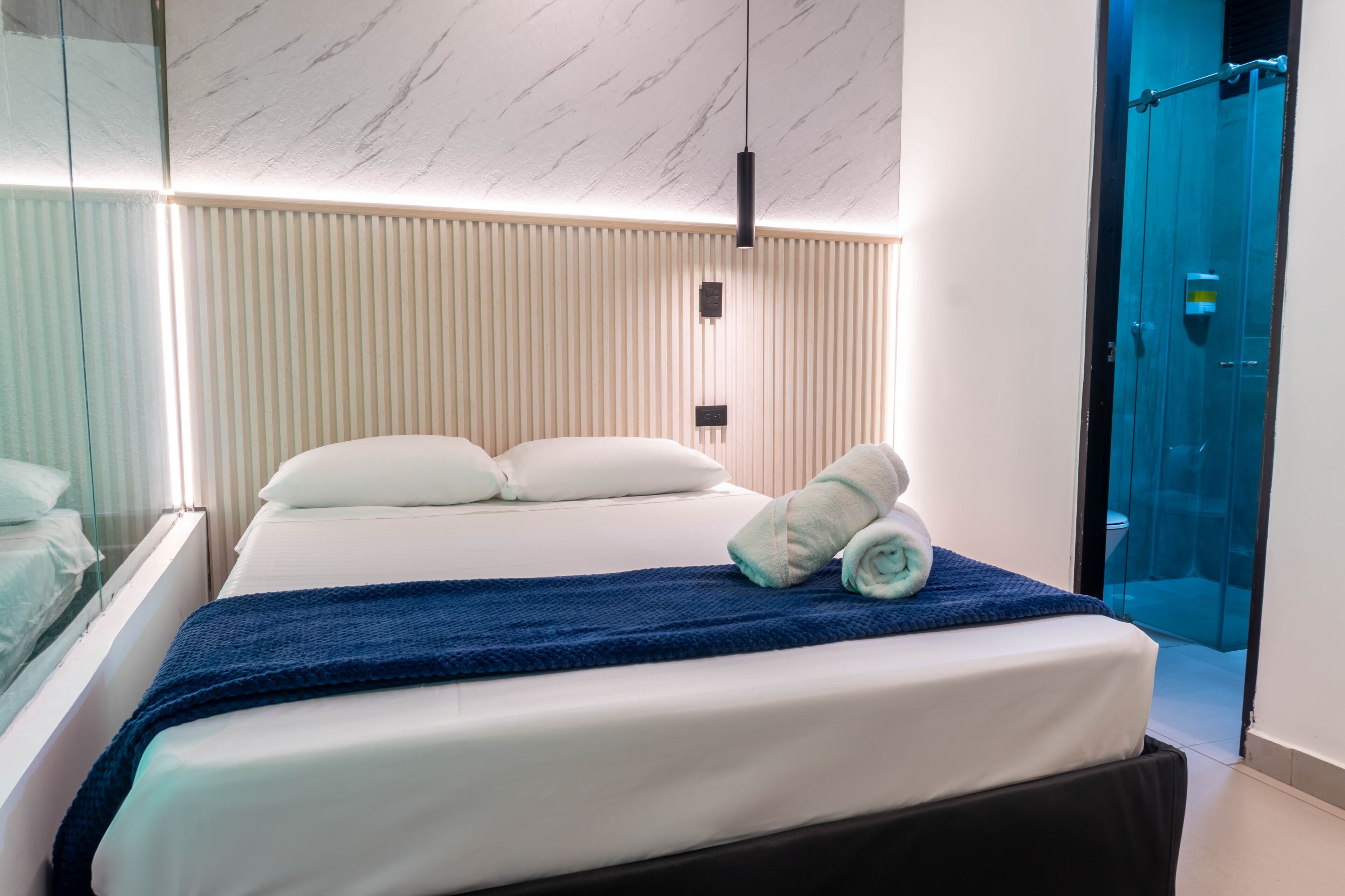Una habitación de hotel moderna con una cama, una manta azul y una toalla.