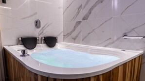 A modern bathroom with a marble-tiled wall, a wooden vanity, a bathtub with a built-in seat, and a handheld showerhead. - hotel civitas medellin (Medellín)