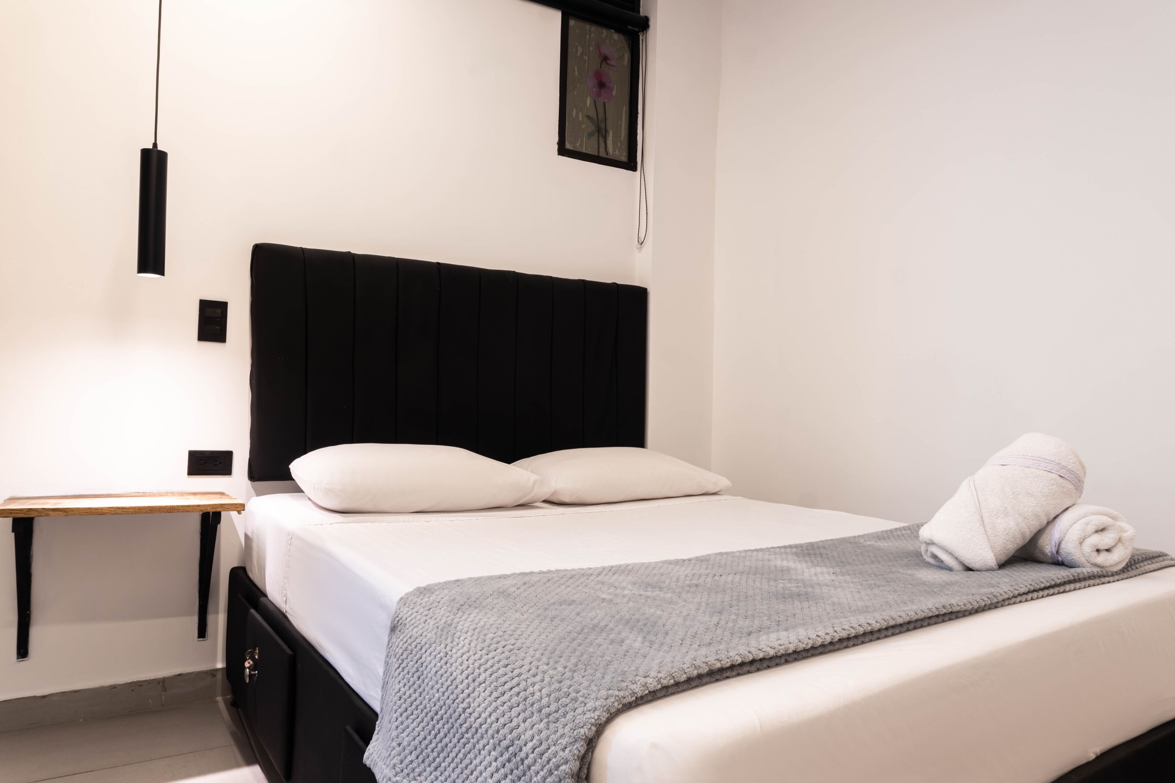 A neatly made bed with a gray blanket, a black headboard, and a white pillow.