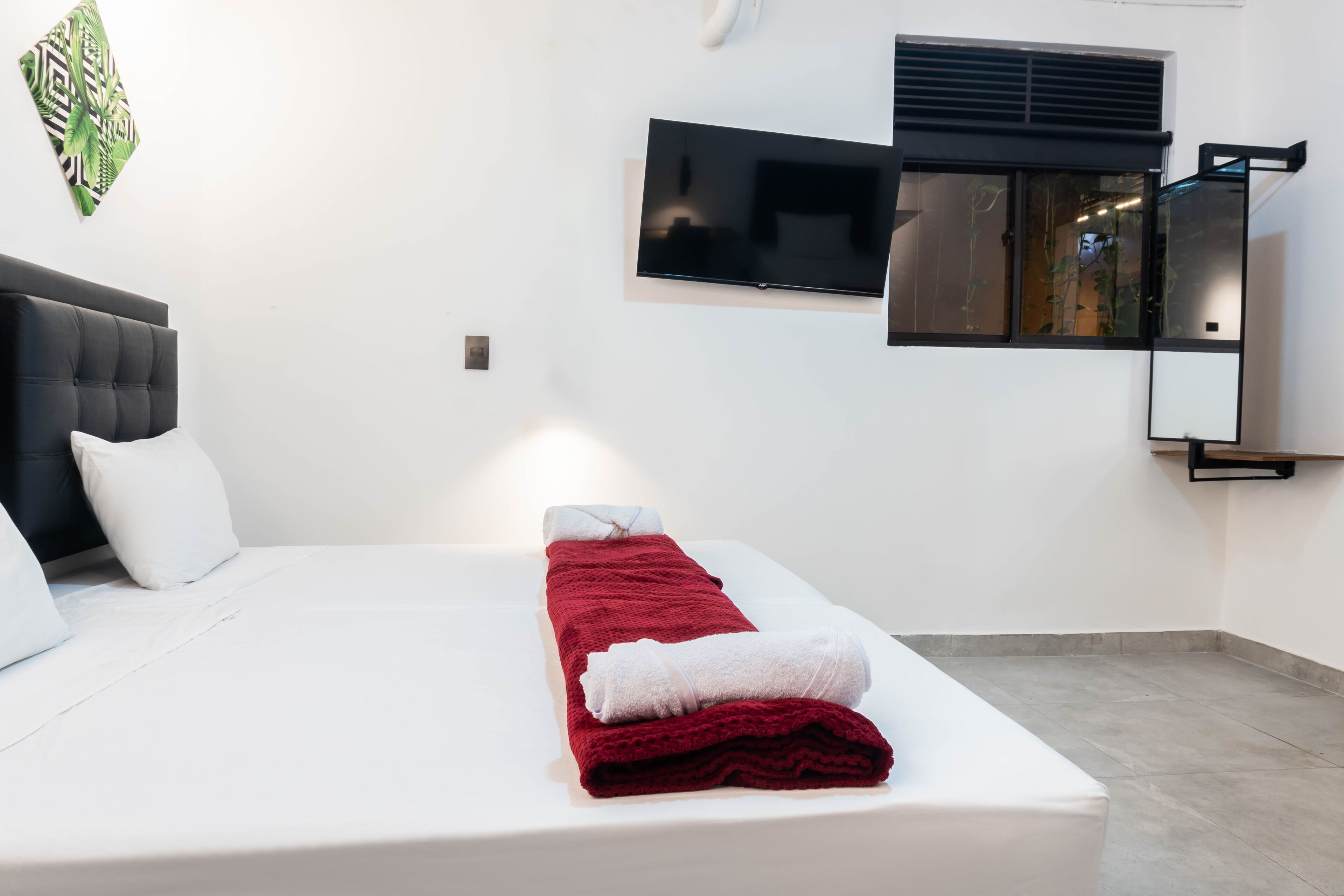 Una habitación de hotel con cama, televisor de pantalla plana, ventana con persianas y aire acondicionado de pared.