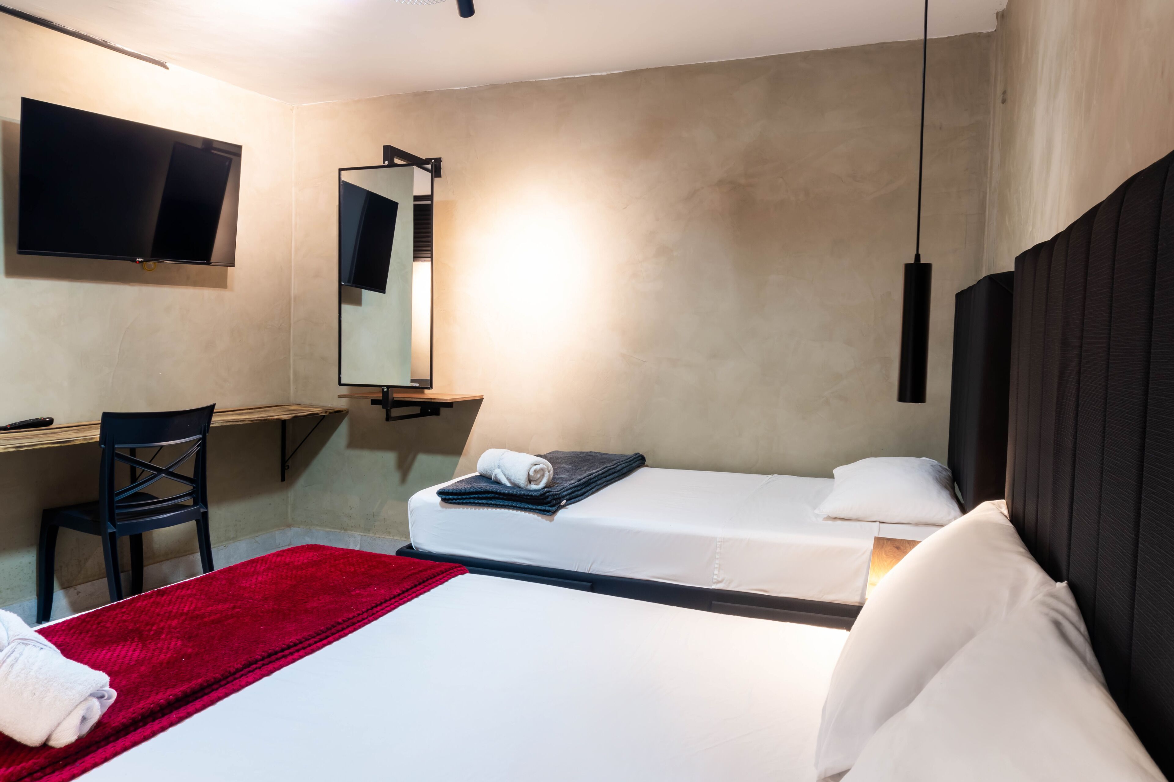 Une chambre d’hôtel avec un lit, un bureau, une chaise, une télévision et un miroir.