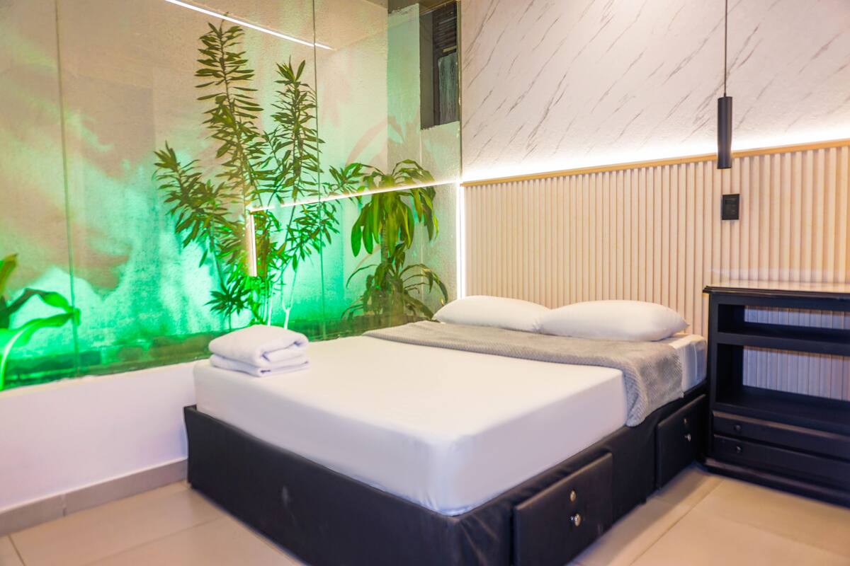 A modern hotel room with a bed, a television, and a large window with a view of the city.