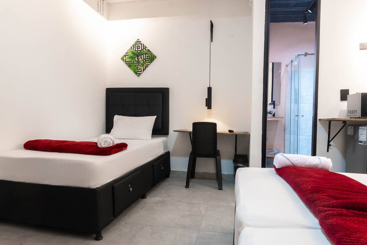 A bedroom with a bed, desk, chair, and a shower area.