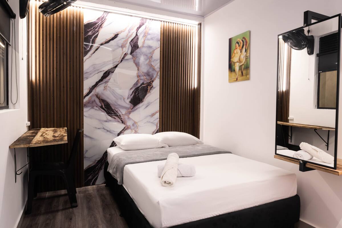 A hotel room with a bed, a desk, a mirror, and a wall with a marble pattern.