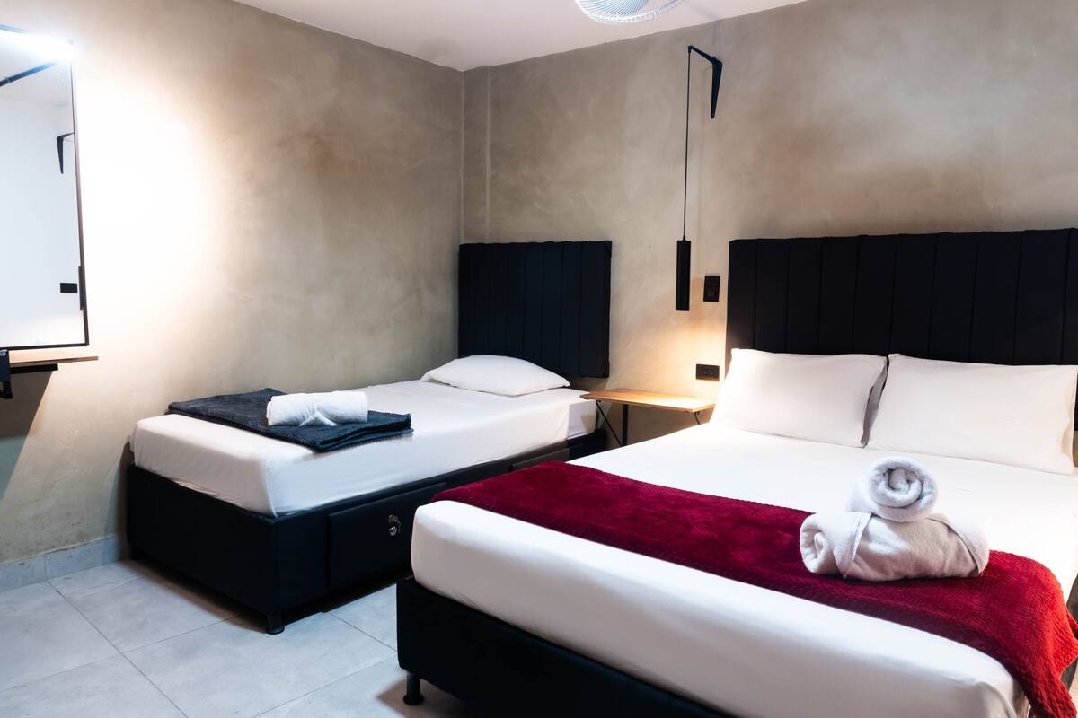 A hotel room with two beds, a red blanket, and a white towel on one bed.