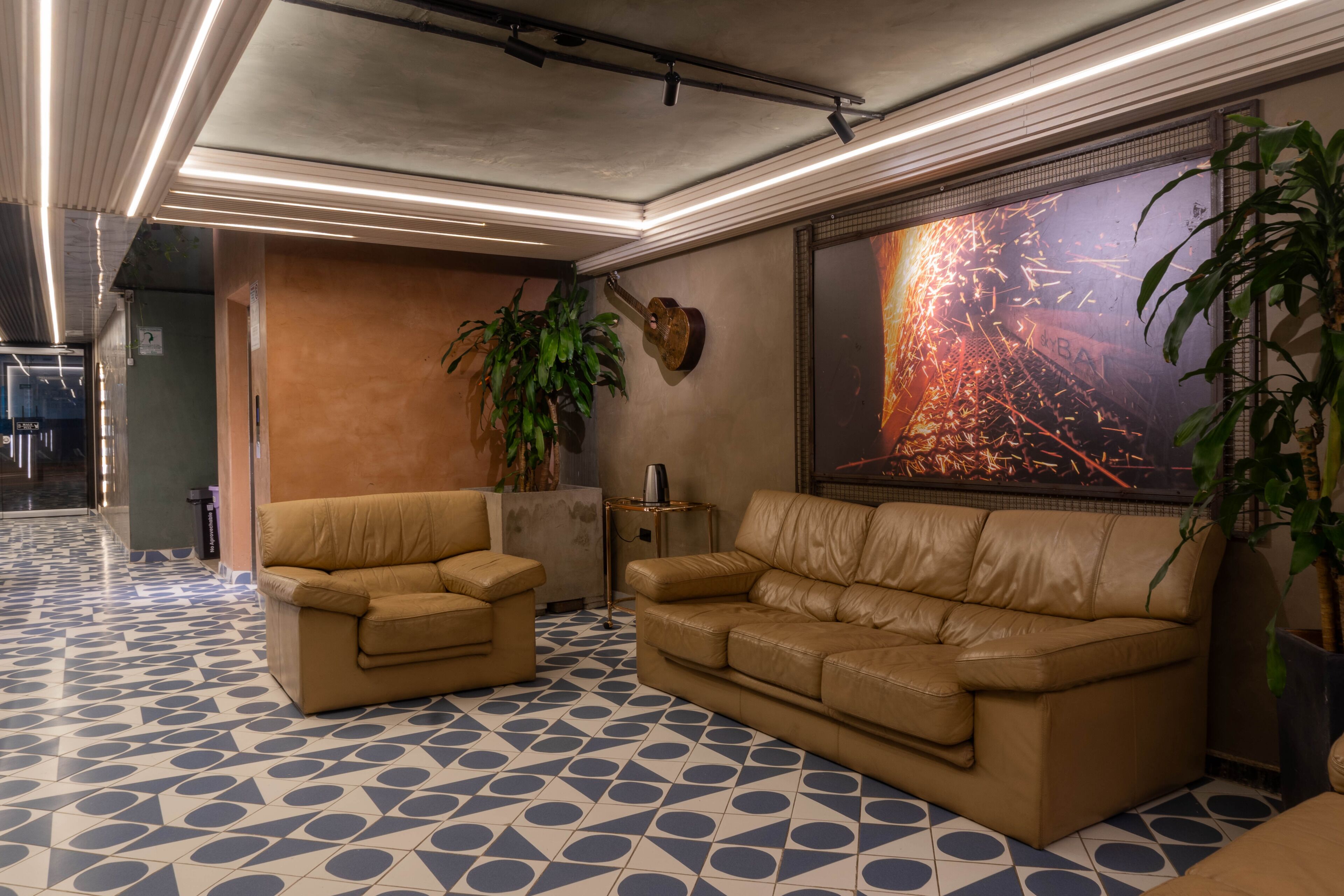 A lobby with two leather sofas, a large abstract painting, a potted plant, and a patterned floor.