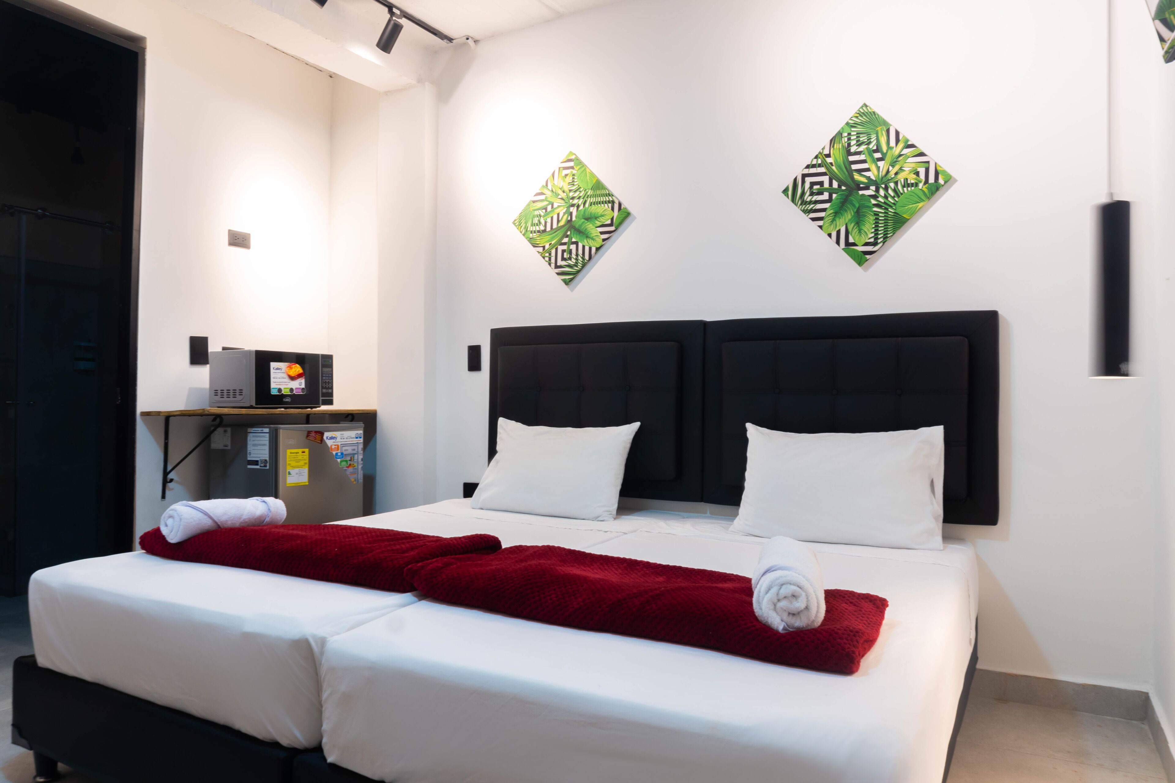 A hotel room with a bed, a desk with a computer, and two wall-mounted artworks.