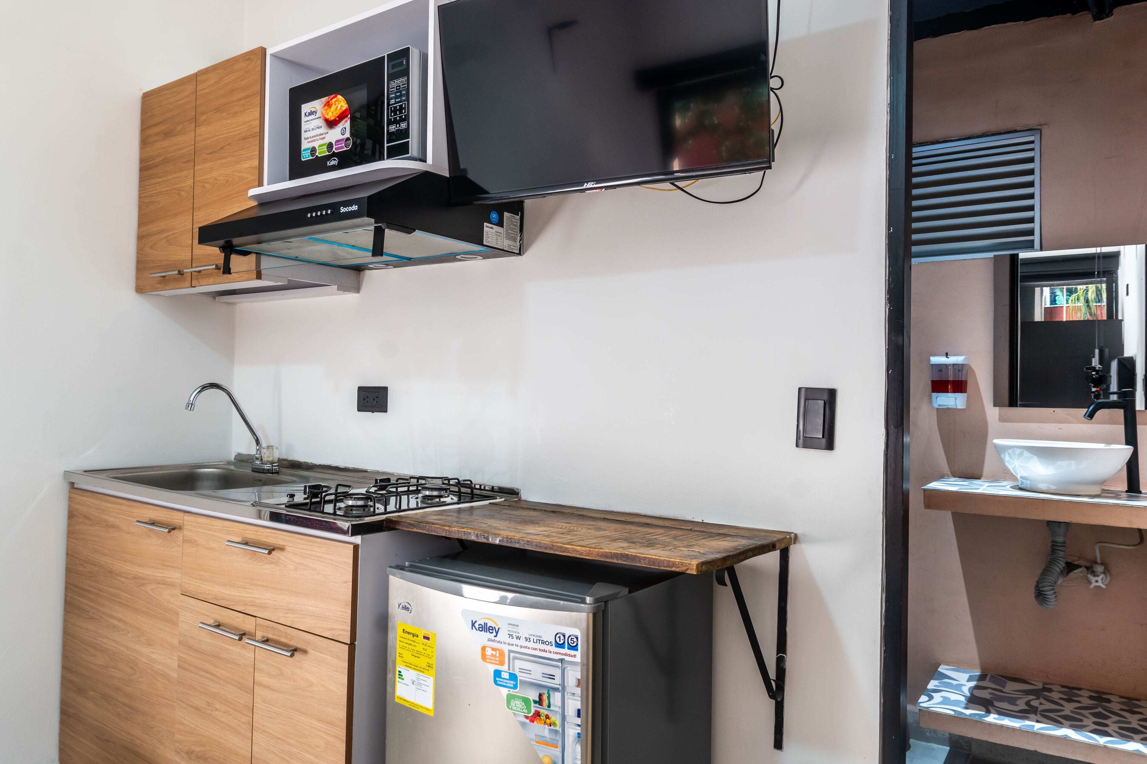 A compact kitchen with a built-in microwave, a gas stove, a refrigerator, wooden cabinets, and a small sink.