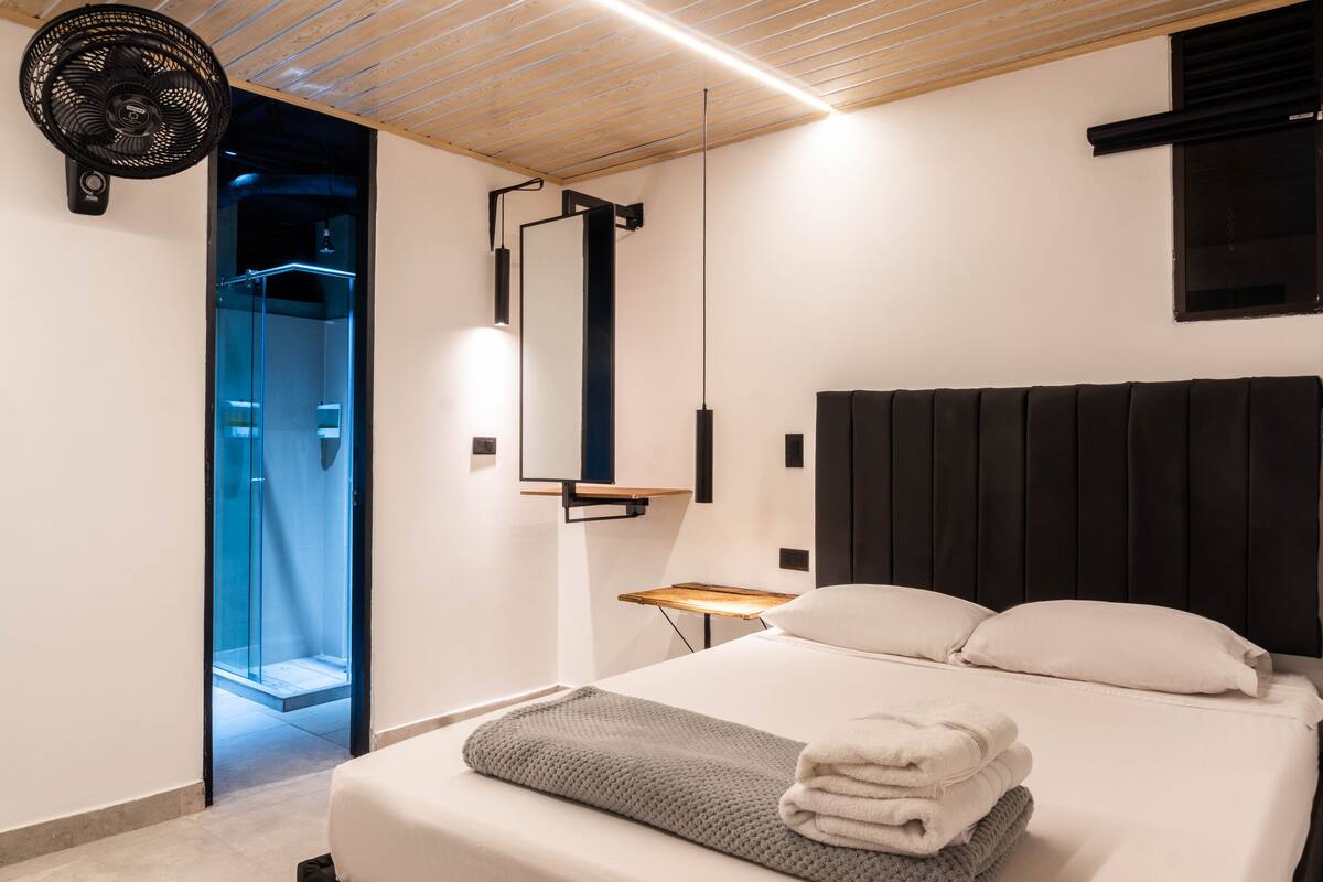 A modern hotel room with a bed, a bedside table, a mirror, and a ceiling fan.