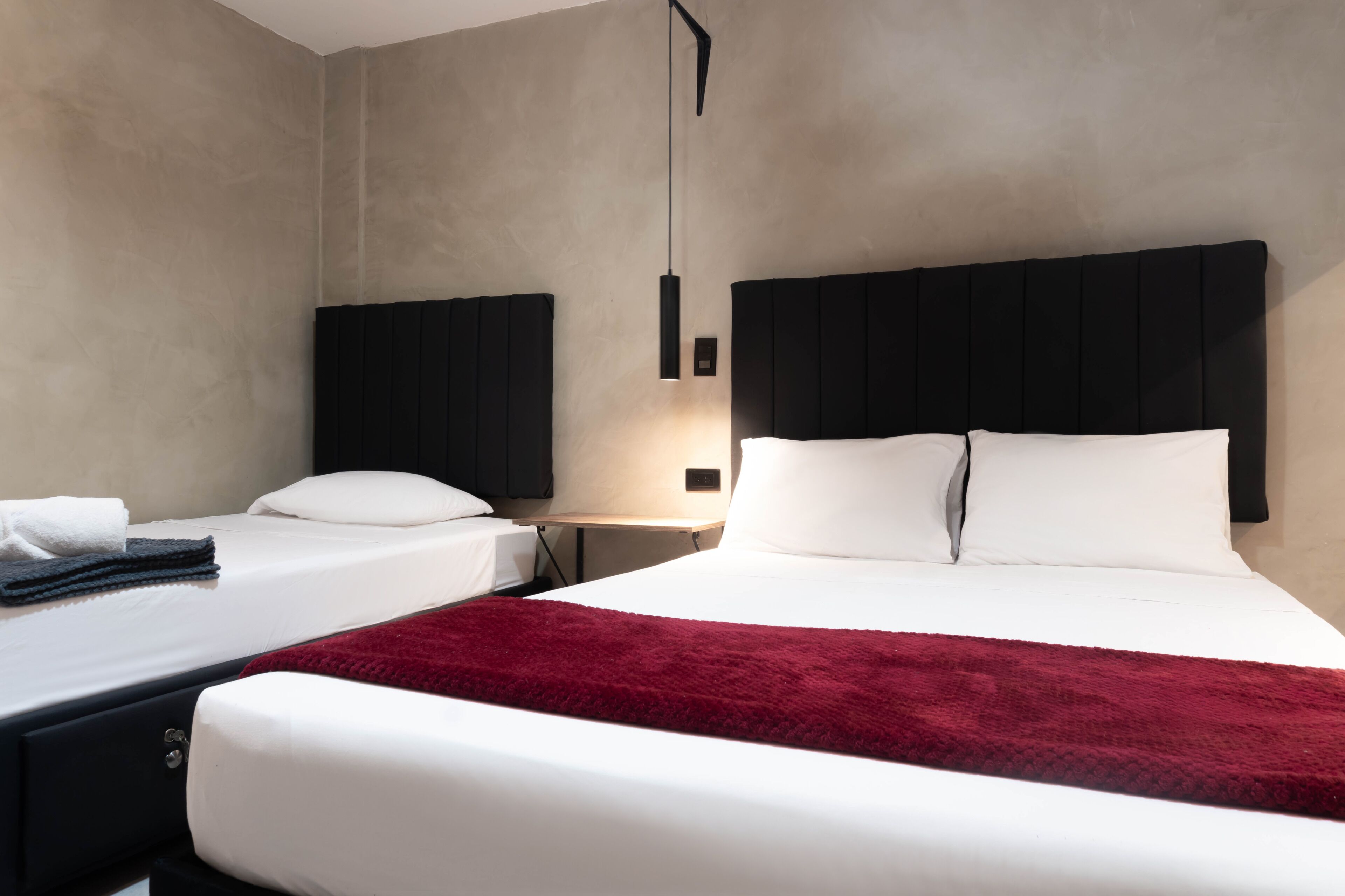 Ein Hotelzimmer mit zwei Betten, einer roten Tagesdecke und einer modernen Pendelleuchte.