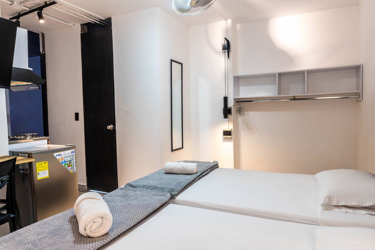 A hotel room with a bed, a small desk, a wall-mounted shelf, and a towel on the bed.