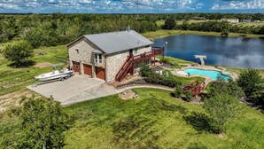 Una casa con fachada de piedra, techo de metal, un muelle, piscina y un lago al fondo.