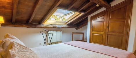 Un dormitorio con techo inclinado, tragaluces, cama con cubrecama acolchado, puerta de madera y radiador.
