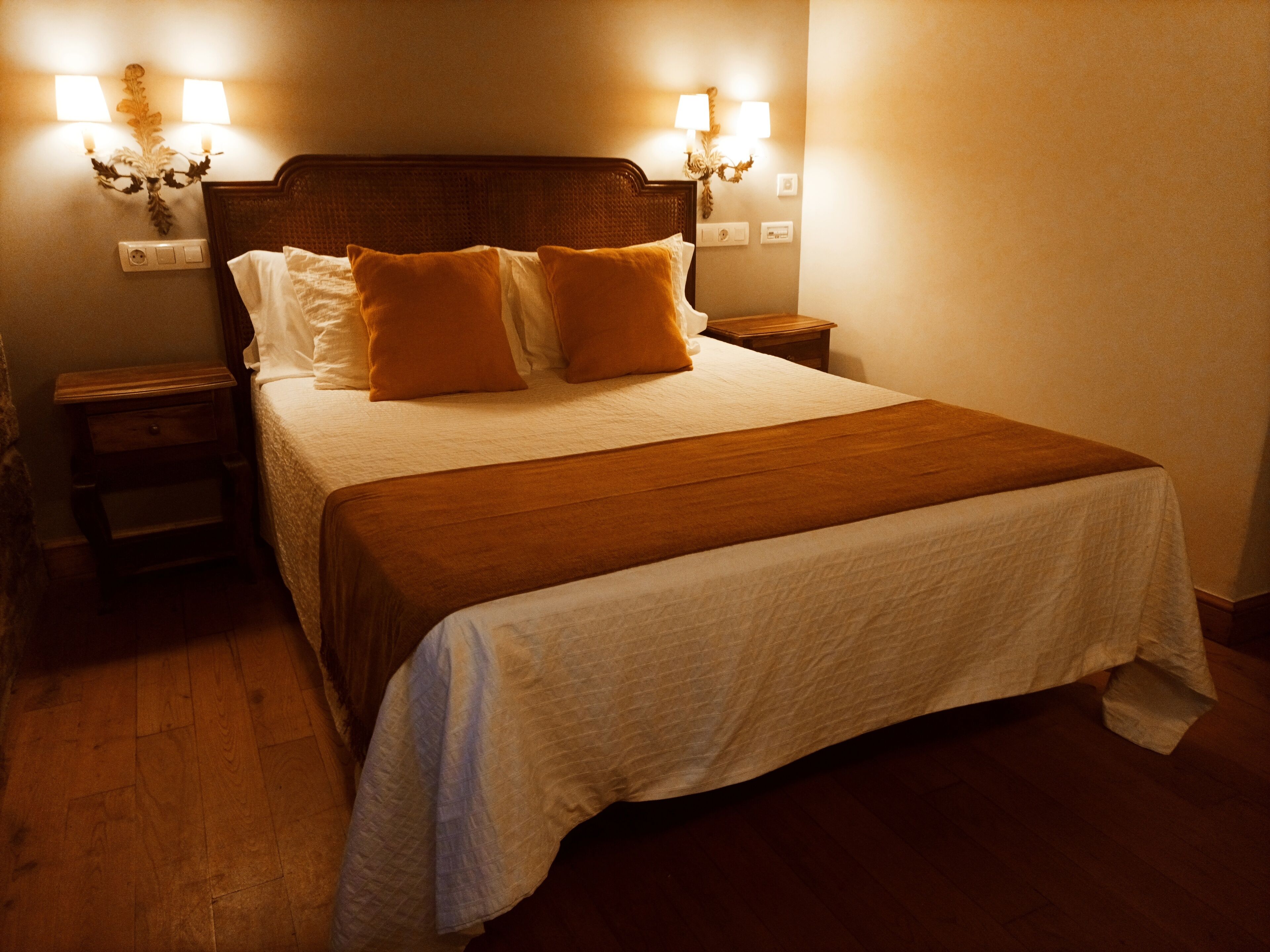 A neatly made bed with a wooden headboard, two bedside tables, and wall-mounted lamps.