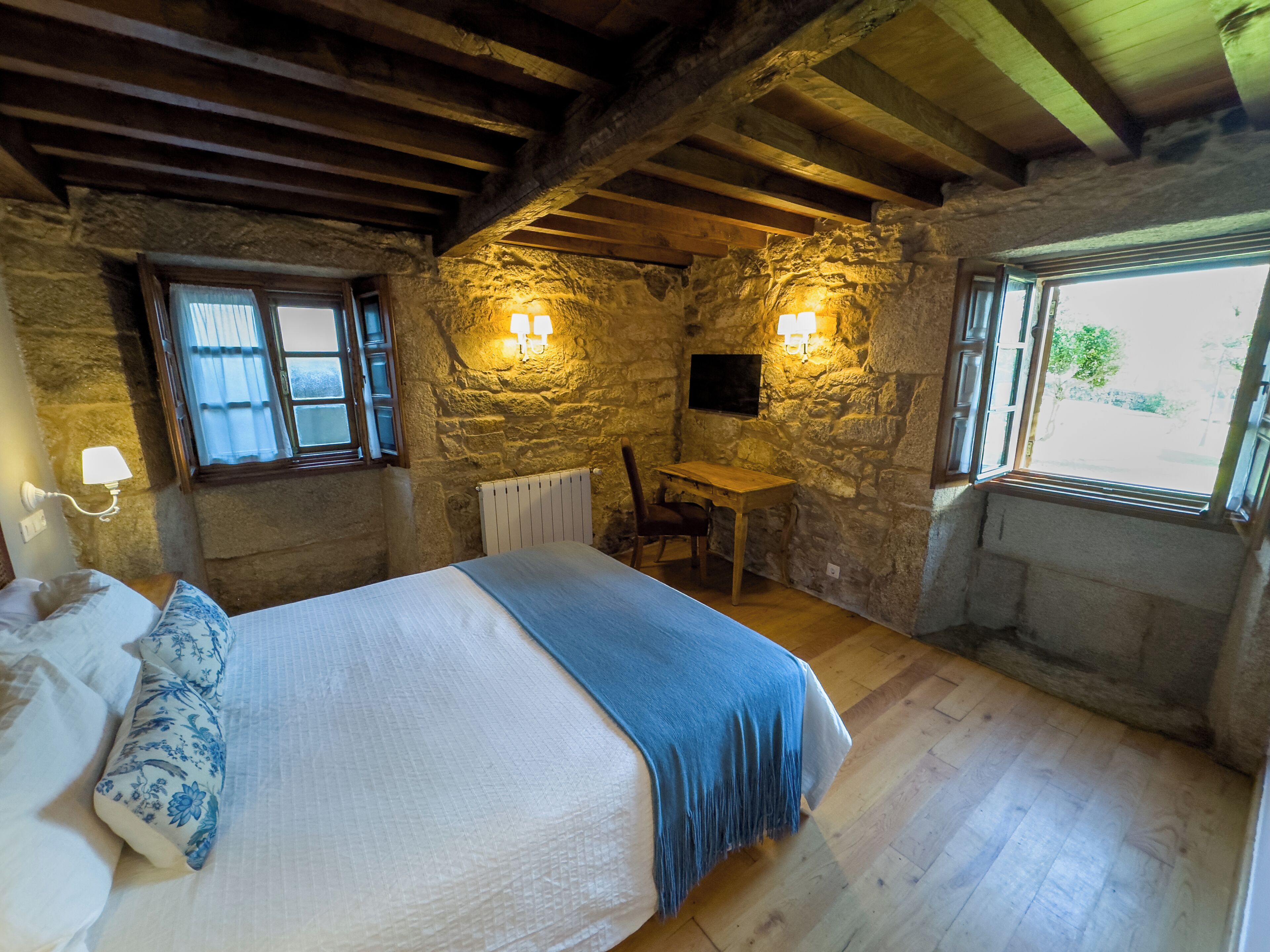 A rustic room with a bed, a desk, and stone walls.