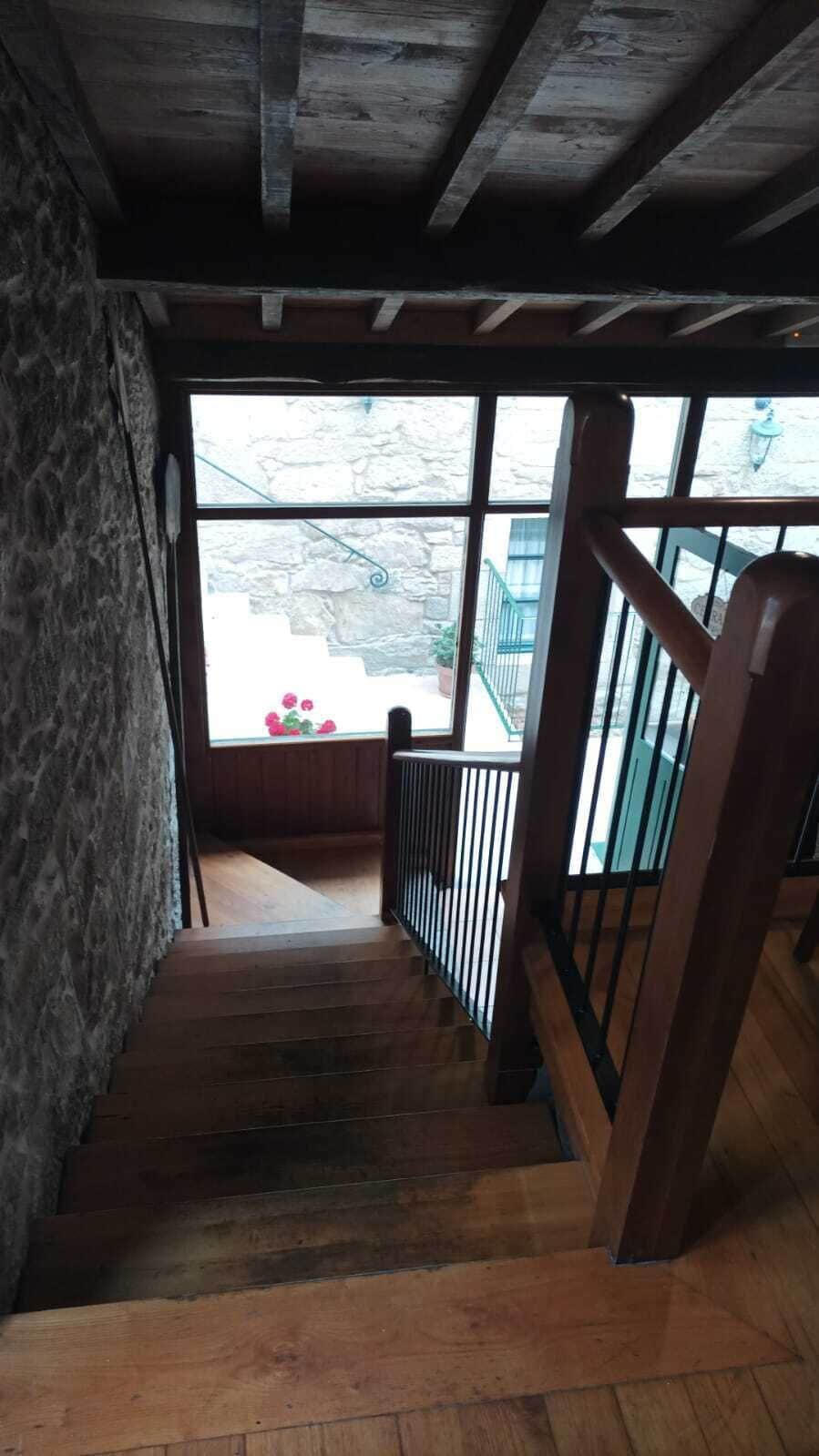 A wooden staircase with a metal railing leading to a balcony with a view of a stone building and a flower arrangement.