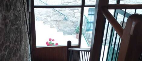 A wooden staircase with a metal railing leading to a balcony with a view of a stone building and a flower arrangement.