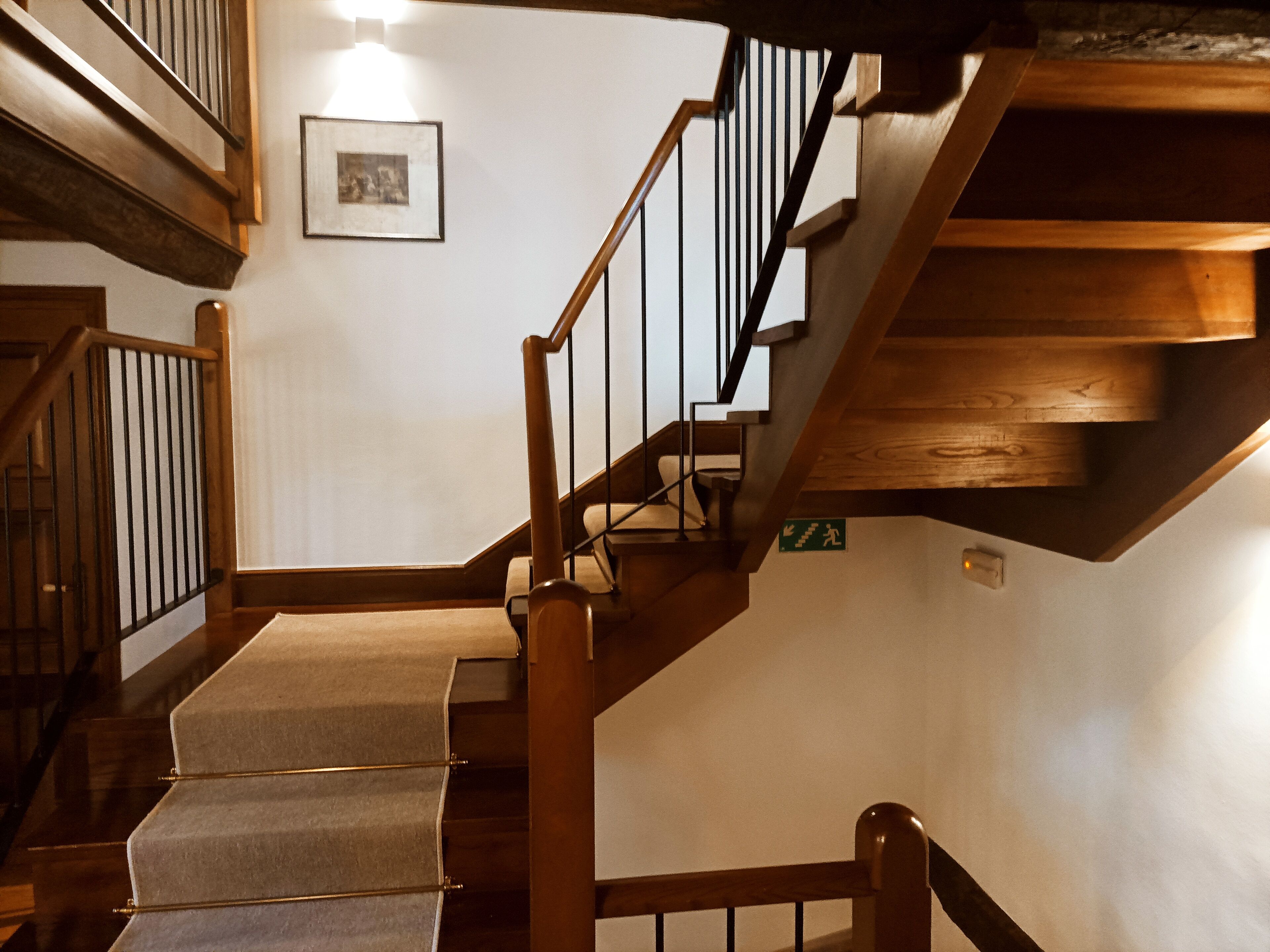A wooden staircase with a handrail, carpeted steps, and a wall-mounted light fixture.