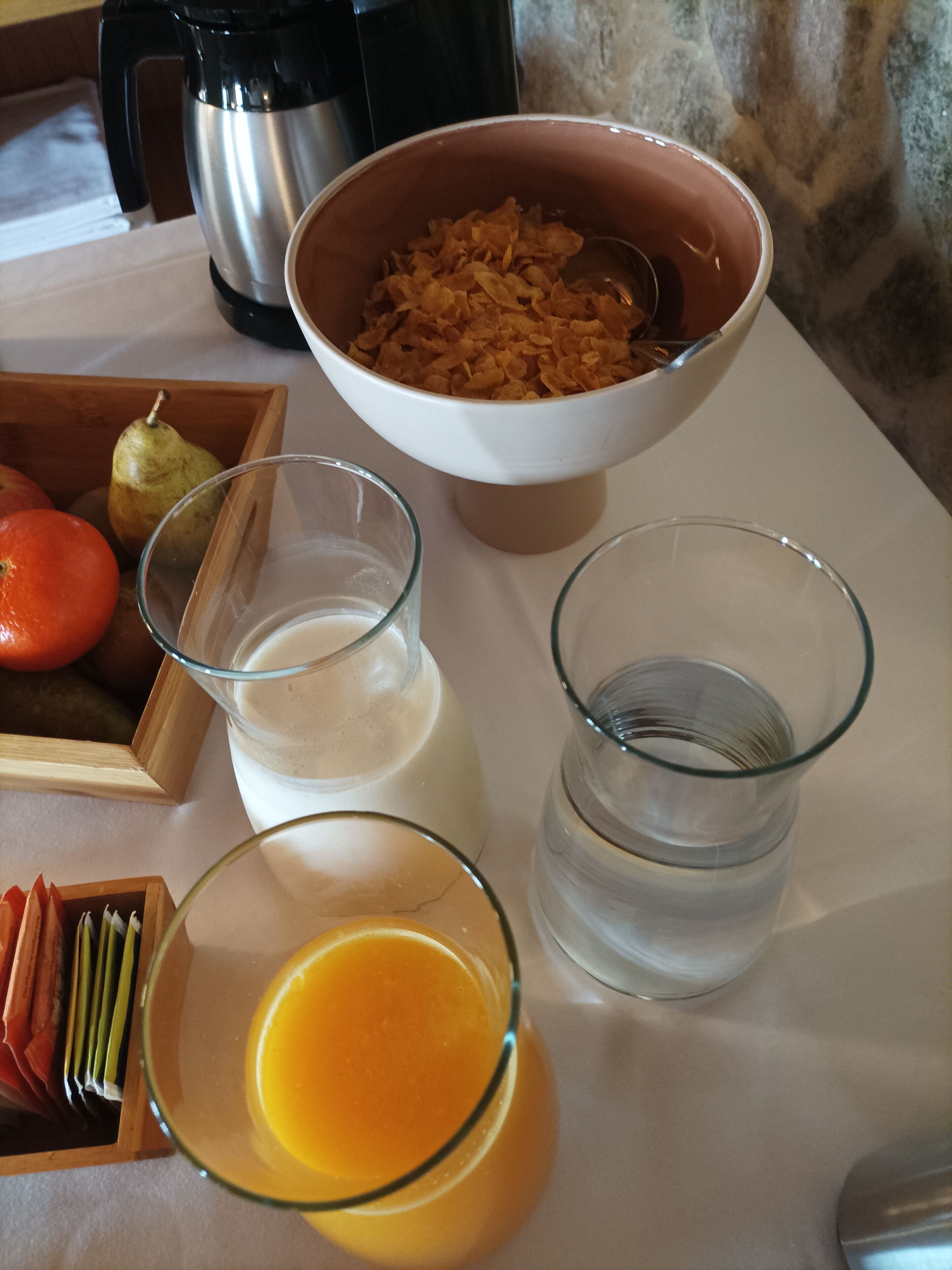 Une table de petit-déjeuner avec un bol de céréales, une cafetière, un verre de lait, un verre d’eau et un verre de jus d’orange.