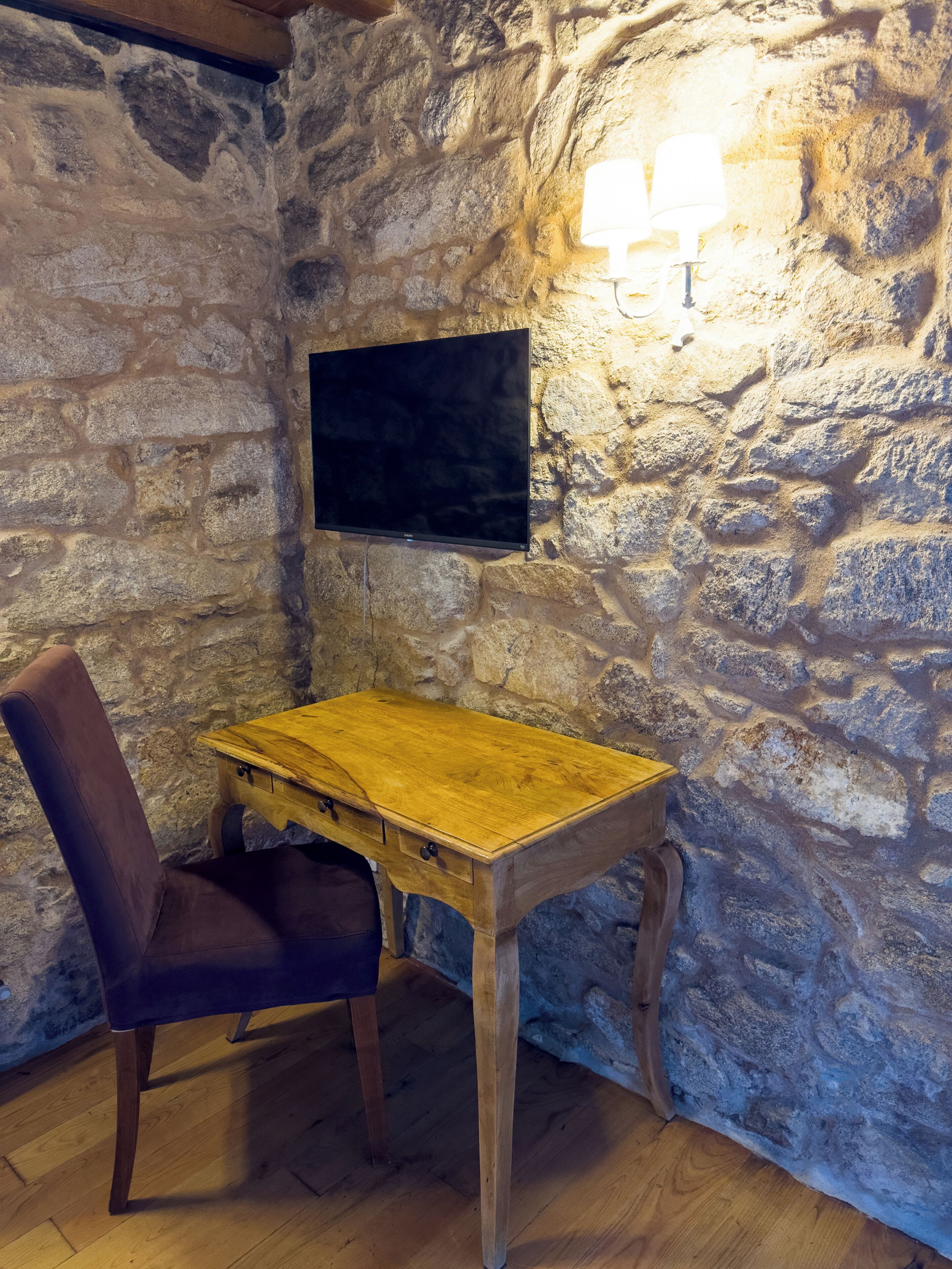Una habitación con paredes de piedra, un escritorio de madera, una silla y un televisor de pantalla plana montado.