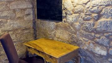 Una habitación con paredes de piedra, un escritorio de madera, una silla y un televisor de pantalla plana montado.