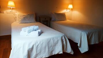 Two single beds with white linens, a wooden nightstand, and wall-mounted lamps.