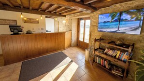 A reception area with a wooden reception desk, a stone wall, a bookshelf with books, a chessboard, and a framed picture of a beach scene.