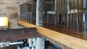 Un interior rústico con pared de piedra, vigas de madera, una zona de bar y una escalera.