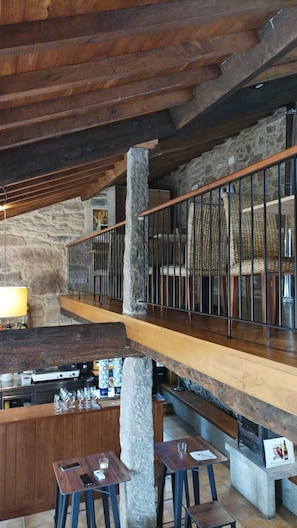 Un interior rústico con pared de piedra, vigas de madera, una zona de bar y una escalera.