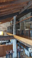 A rustic interior with a stone wall, wooden beams, a bar area, and a staircase.