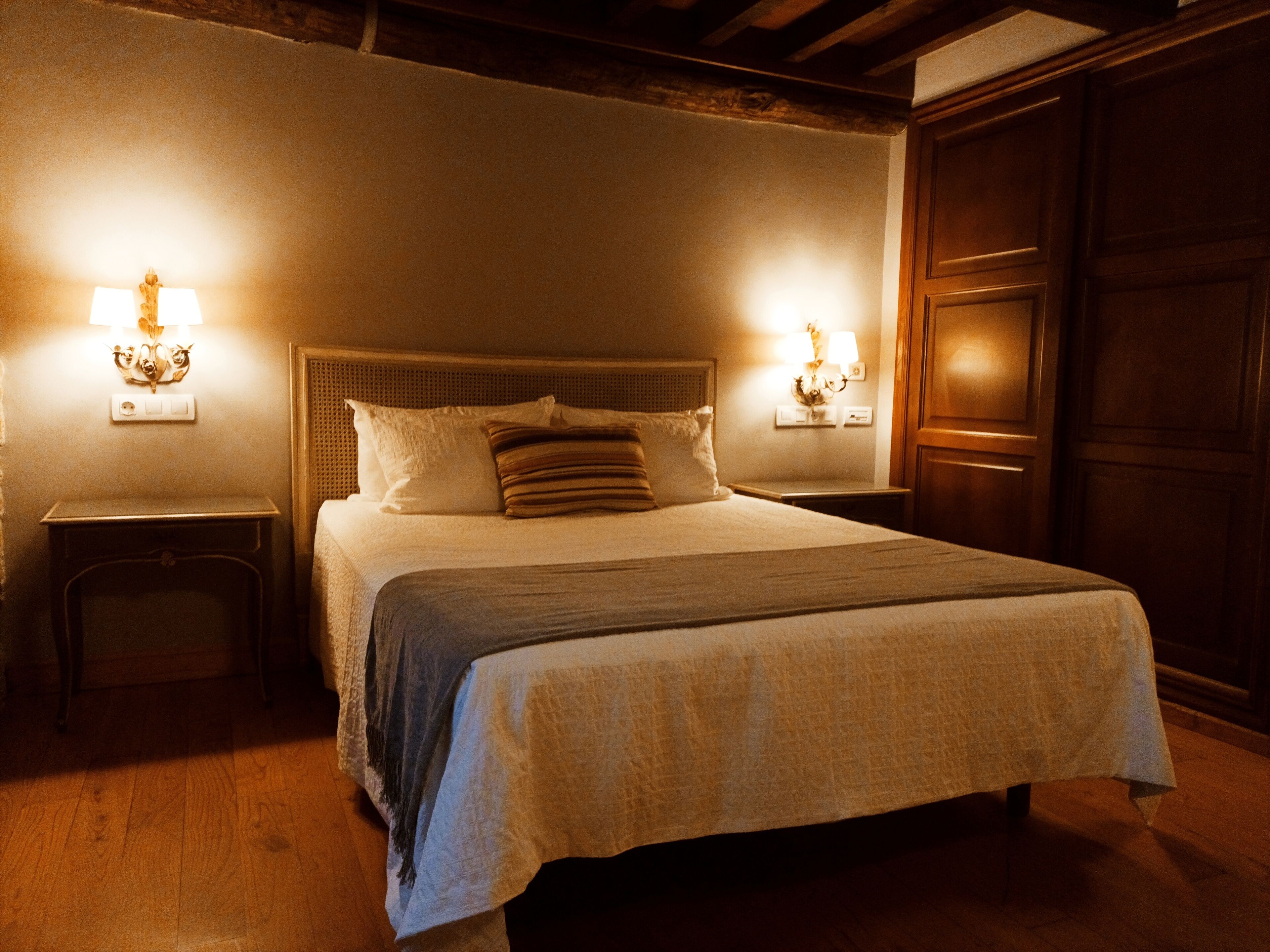 Una cama bien hecha con cabecera, dos mesitas de noche y lámparas de pared.
