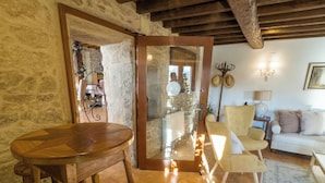 A rustic interior with a wooden table and chairs, stone walls, and a tiled floor.