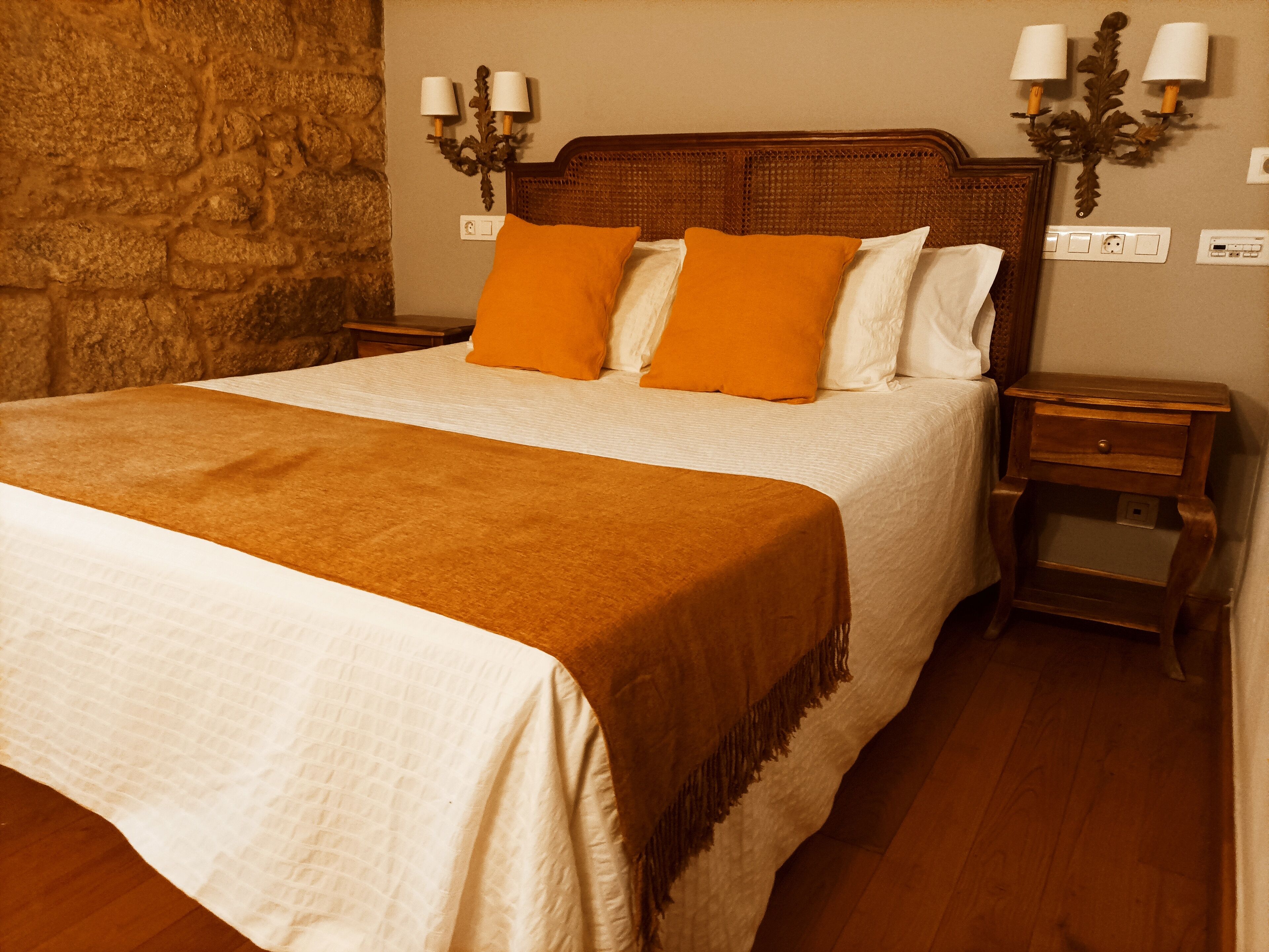 A neatly made bed with a brown blanket, white linens, and two orange pillows.