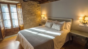A bedroom with a large bed, wooden beams, stone wall, and two bedside lamps.