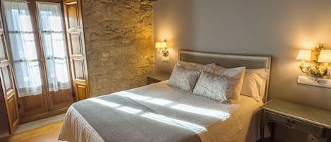 A bedroom with a large bed, wooden beams, stone wall, and two bedside lamps.