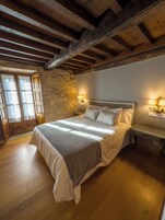 A bedroom with a large bed, wooden beams, stone wall, and two bedside lamps.