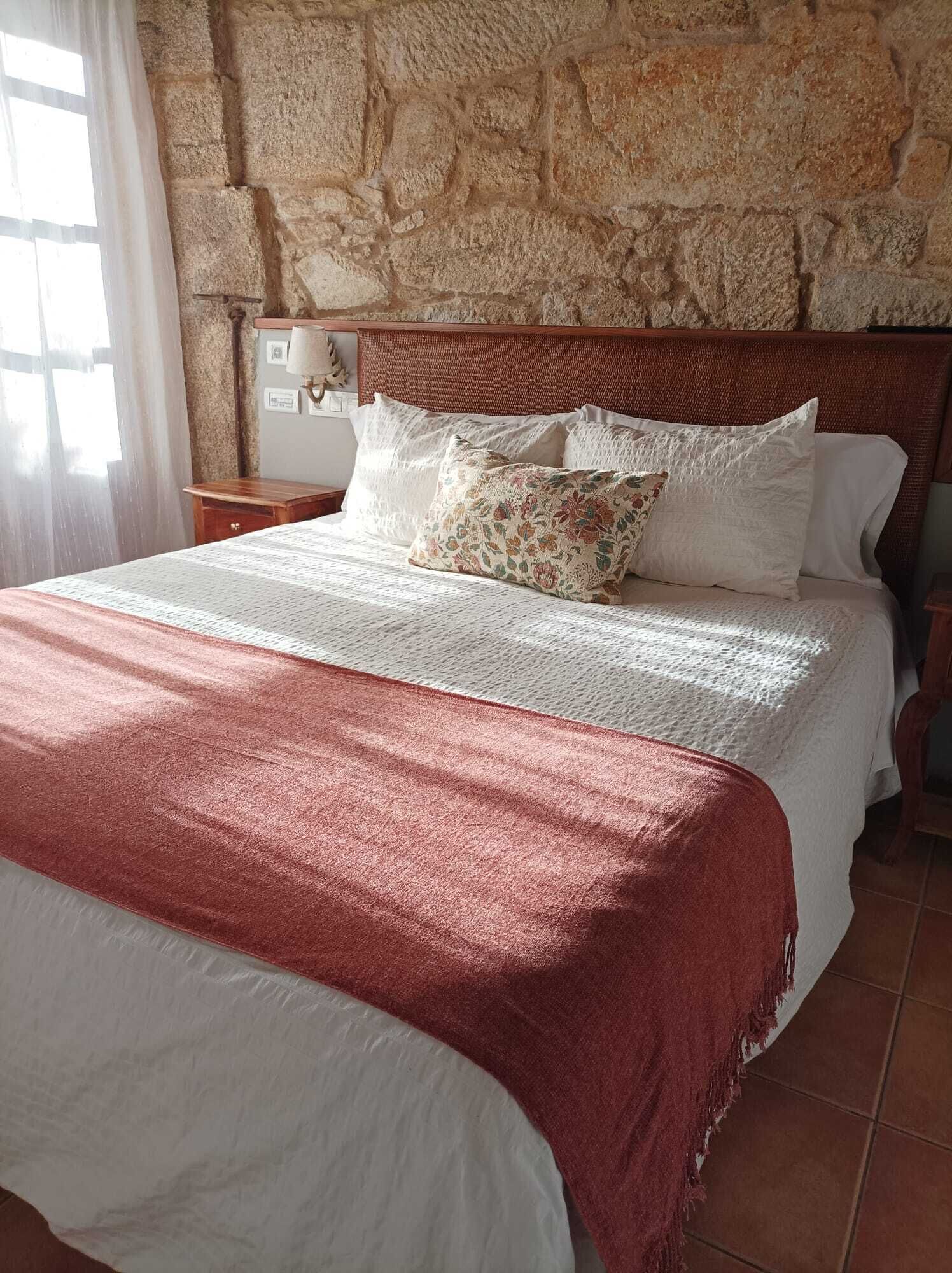 Ein Bett mit Holz-Kopfteil, weißer Bettwäsche und einer roten Tagesdecke.
