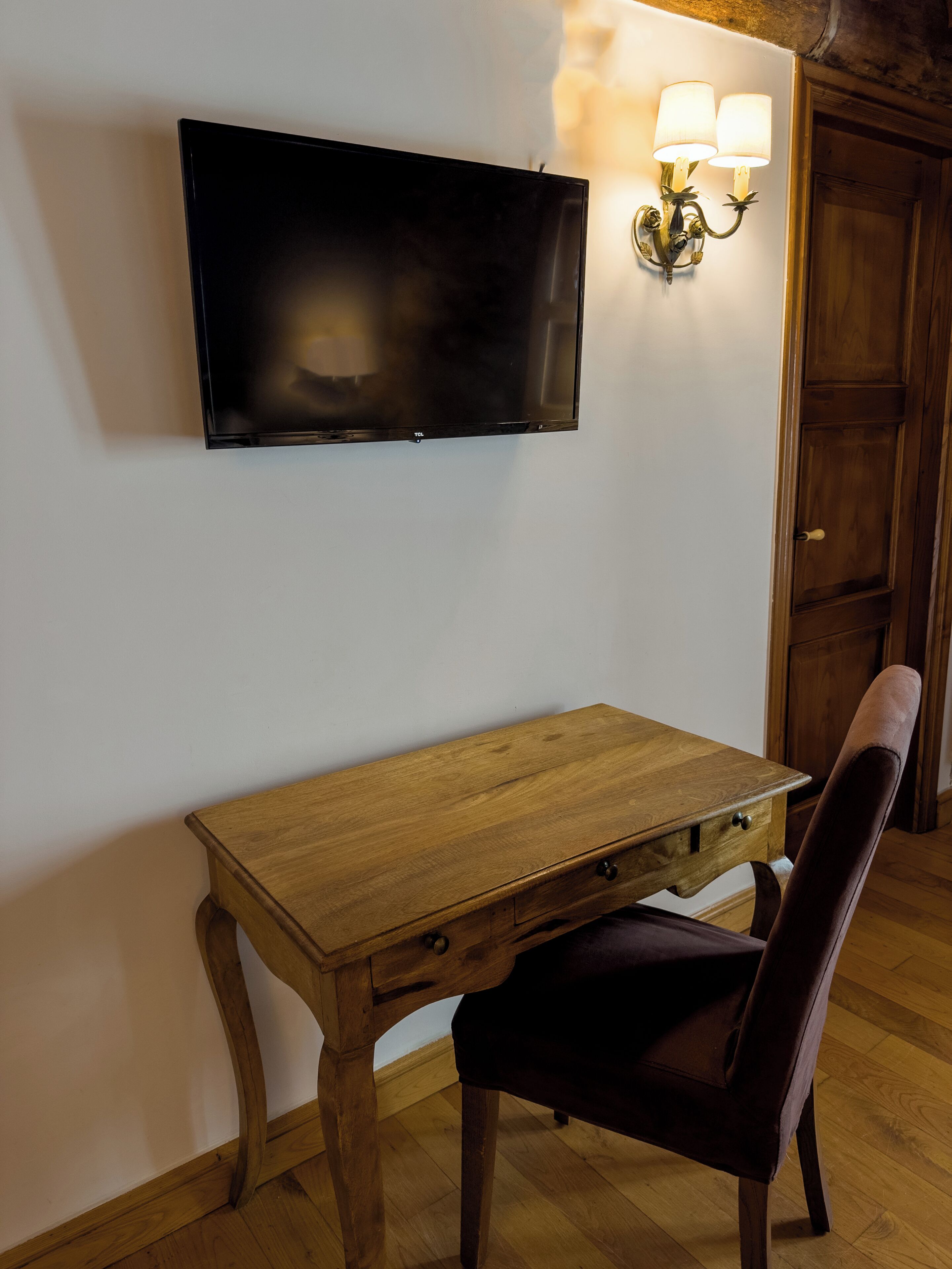 Ein Holztisch mit einem an der Wand montierten Fernseher, ein Stuhl und eine Wandlampe.