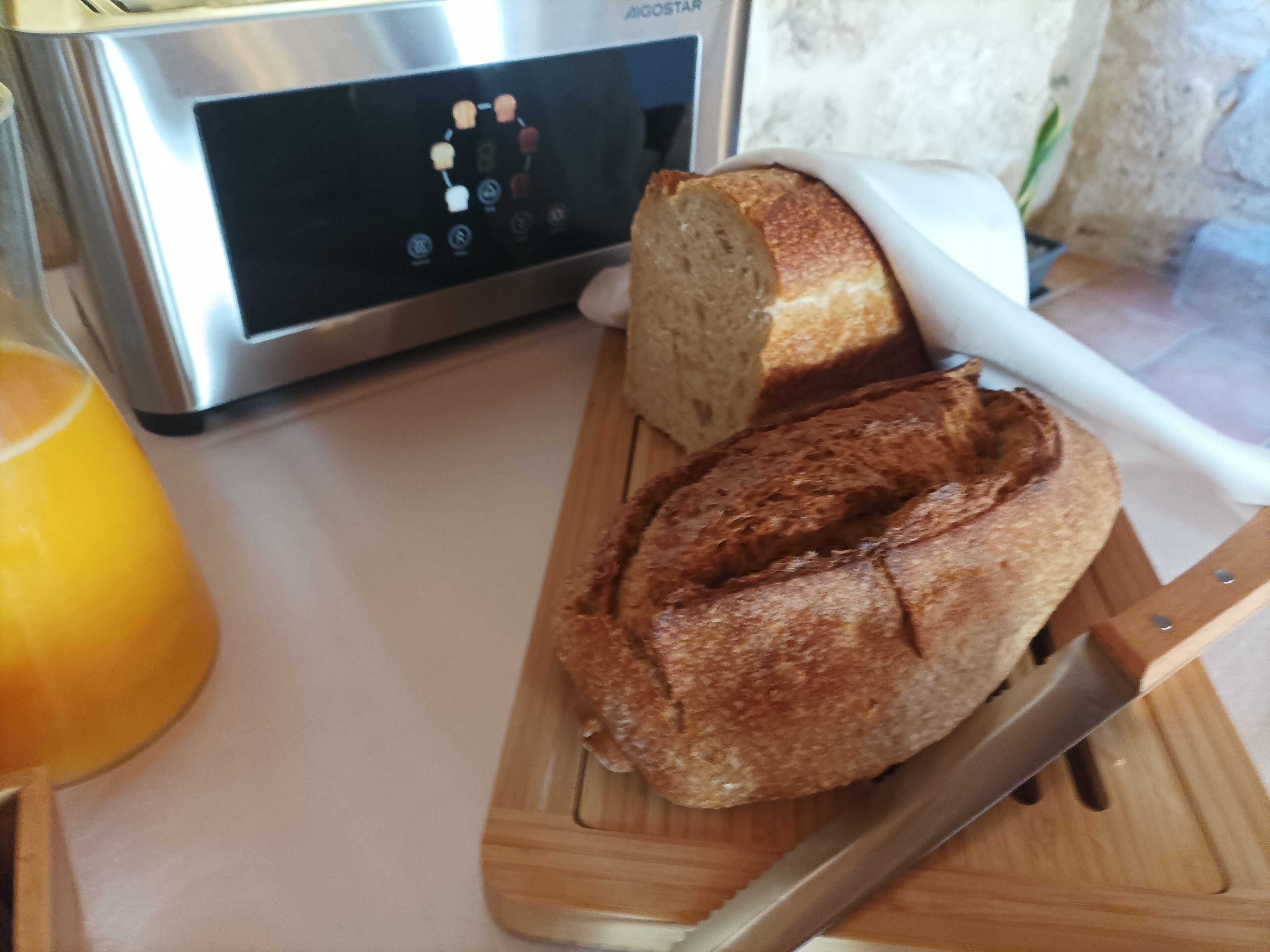 A loaf of bread on a wooden cutting board with a knife beside it, placed on a kitchen counter.
